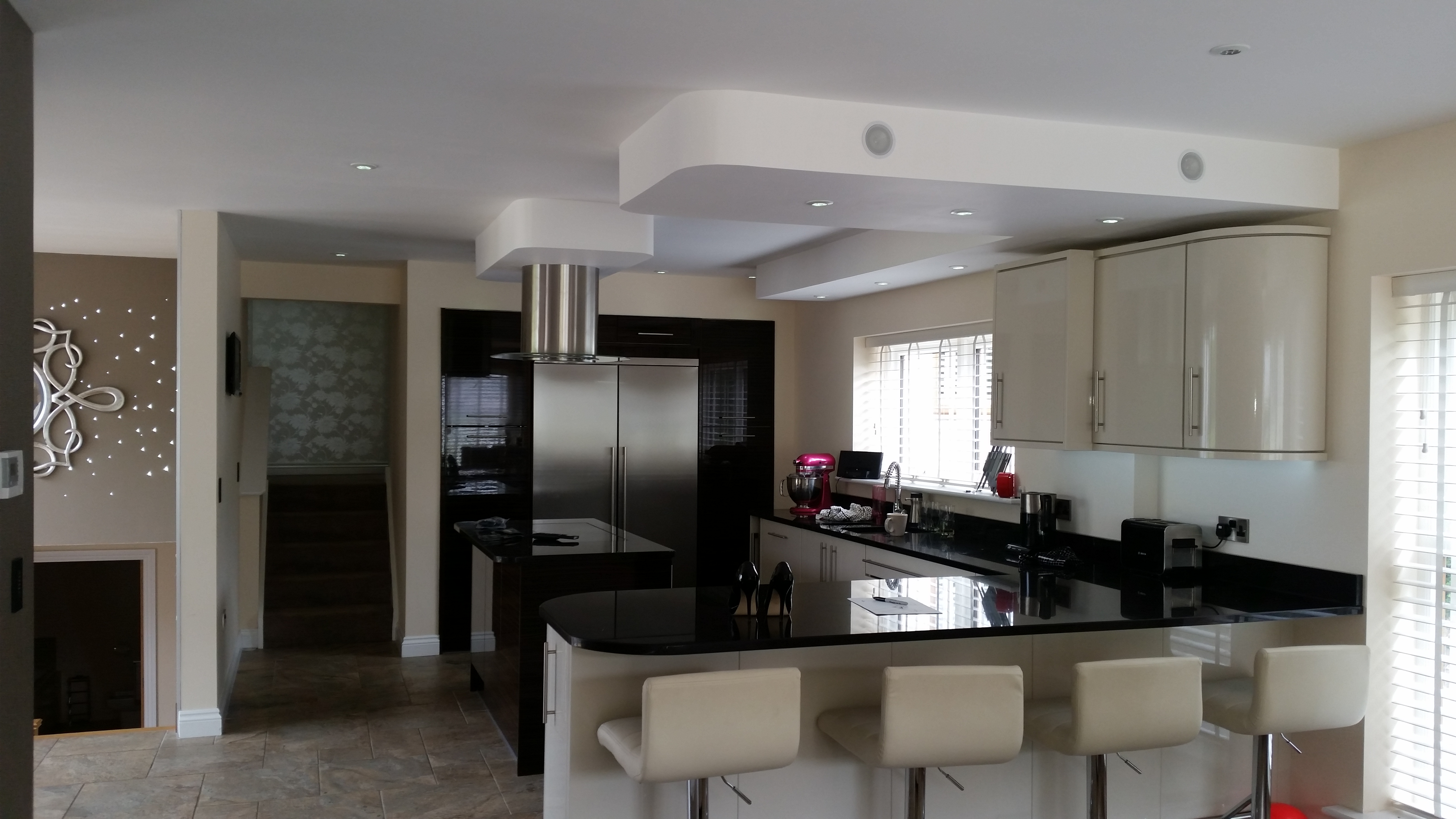 Wide view of a kitchen with a dark central island, pale cabinetry and bar seating