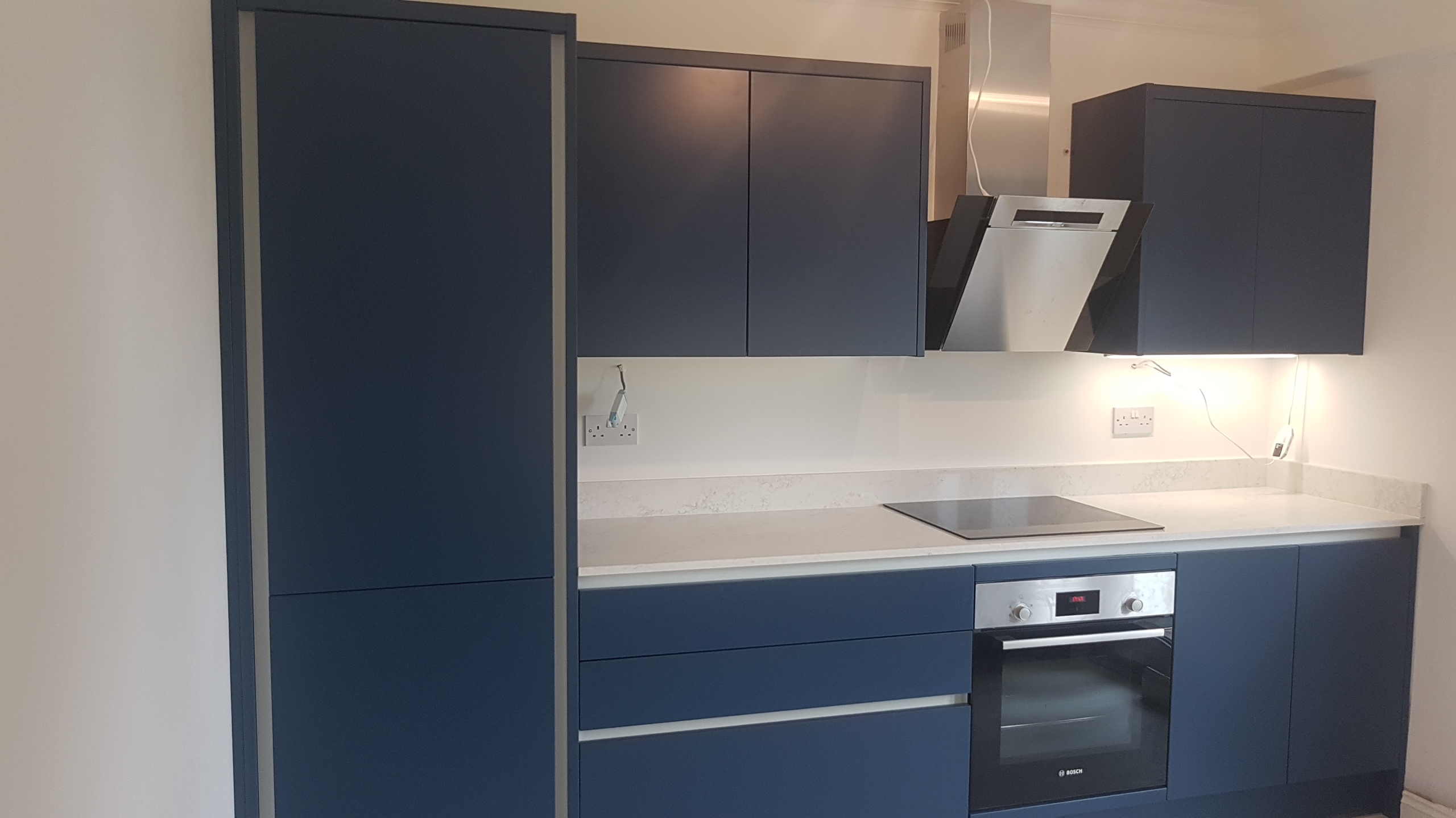 Dark blue kitchen cabinetry with light worktops and a built-in oven