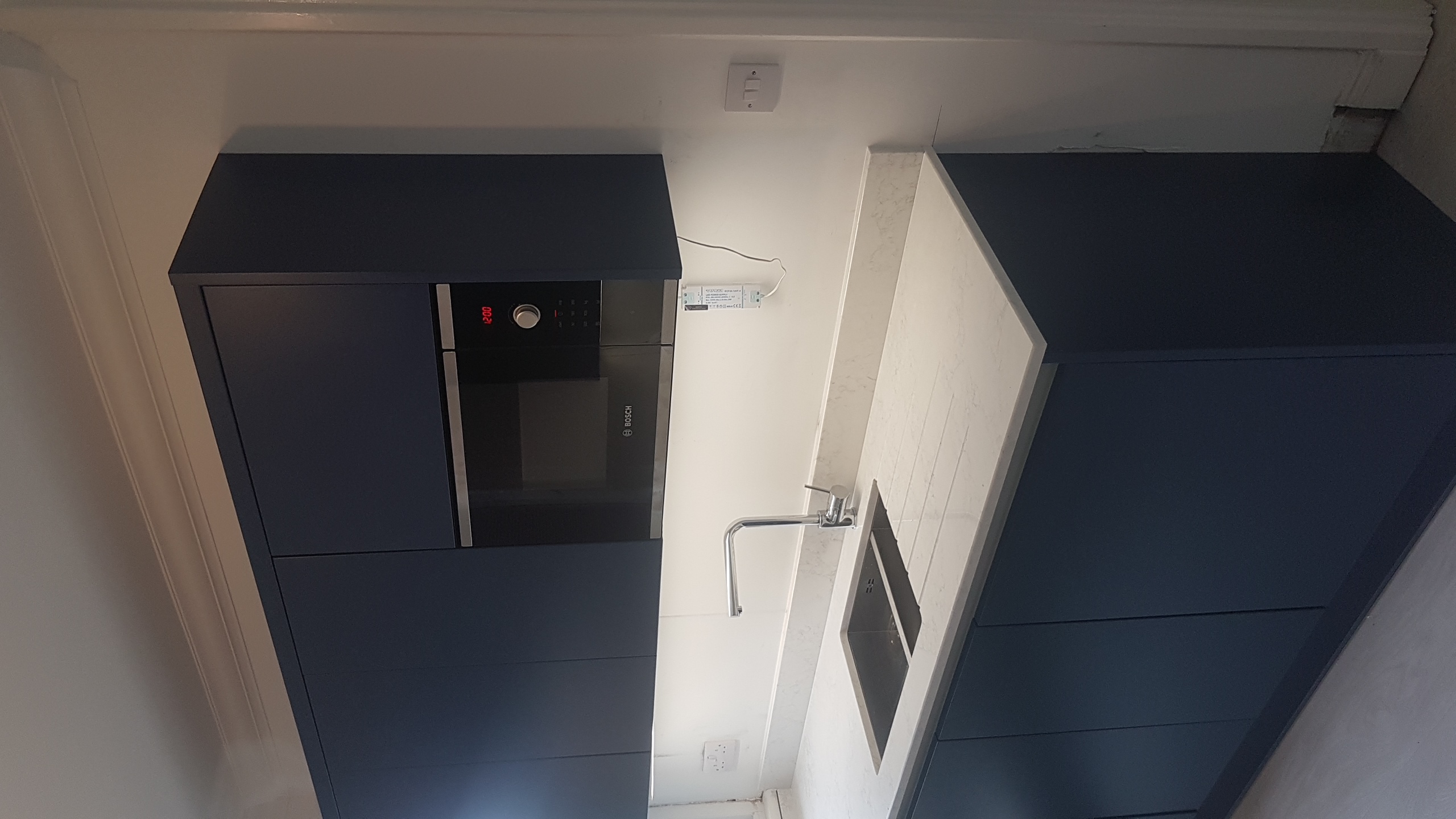 Close view of dark blue cabinets, sink area and pale worktops