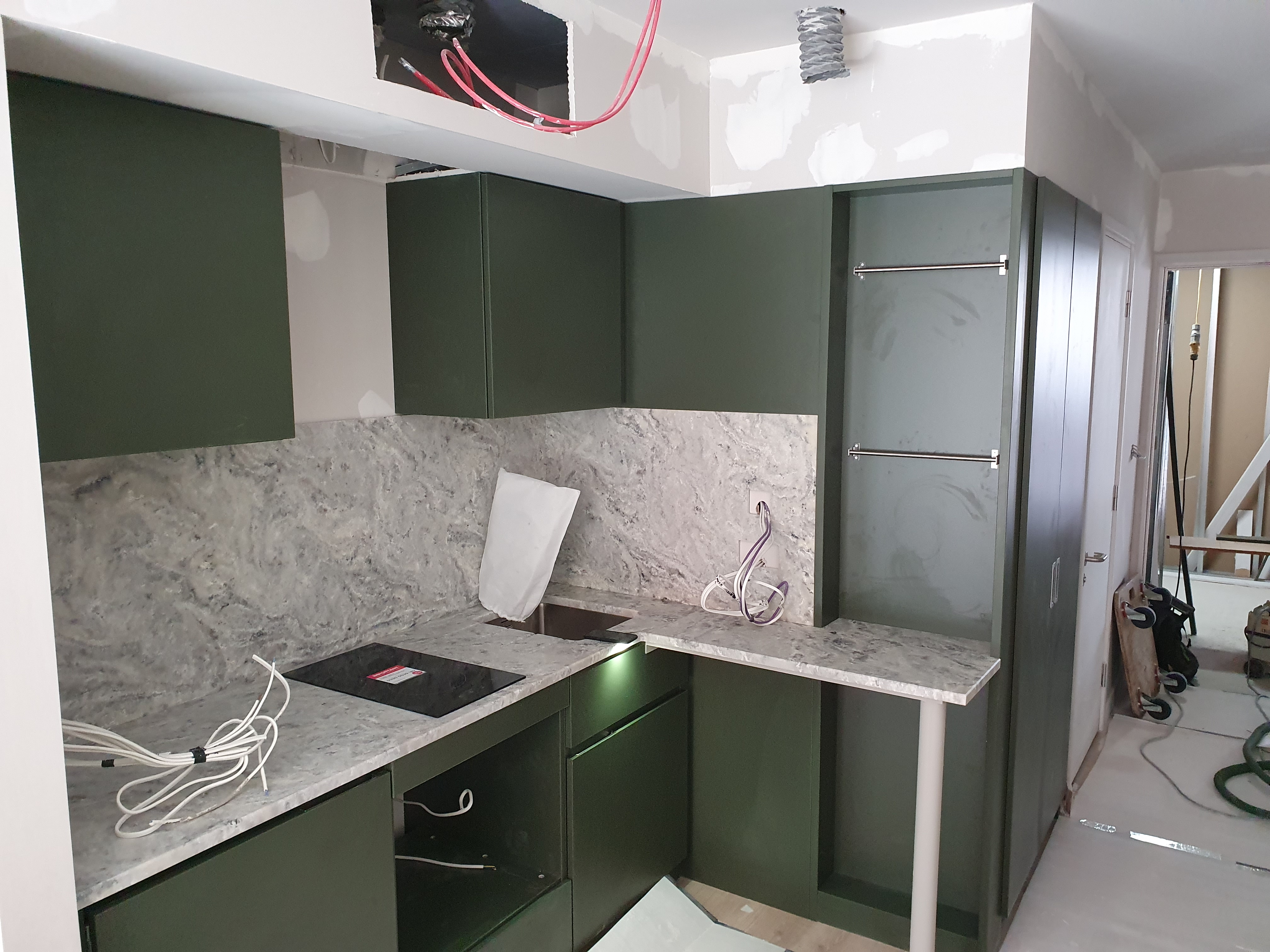 Light grey kitchen cabinetry with pale marble-patterned worktops and unfinished floor area